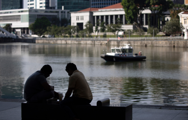 Dos hombres sentados junto al río Singapur frente a la Casa del Parlamento.