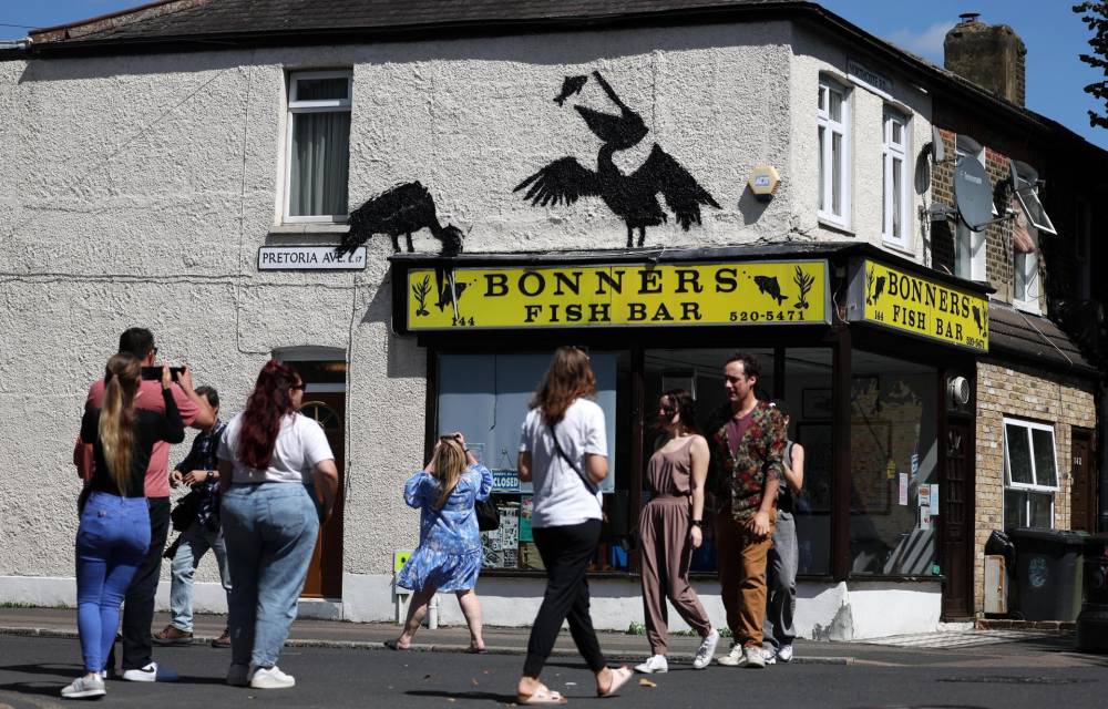 La gente observa una obra de arte recientemente confirmada de Banksy en el costado de una tienda de pescado y papas fritas en Walthamstow en Londres, Gran Bretaña, el 9 de agosto de 2024. Es la quinta obra de arte animal confirmada de Banksy en el espacio de cinco días. (Reino Unido, Londres) EFE/EPA/ANDY LLUVIA