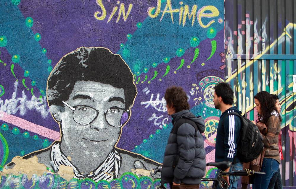 Fotografía de archivo del 13 de agosto de 2014 que muestra a un grupo de personas caminando frente a un mural con la imagen del asesinado abogado, activista por la paz y popular humorista de la televisión colombiana Jaime Garzón en Bogotá (Colombia).