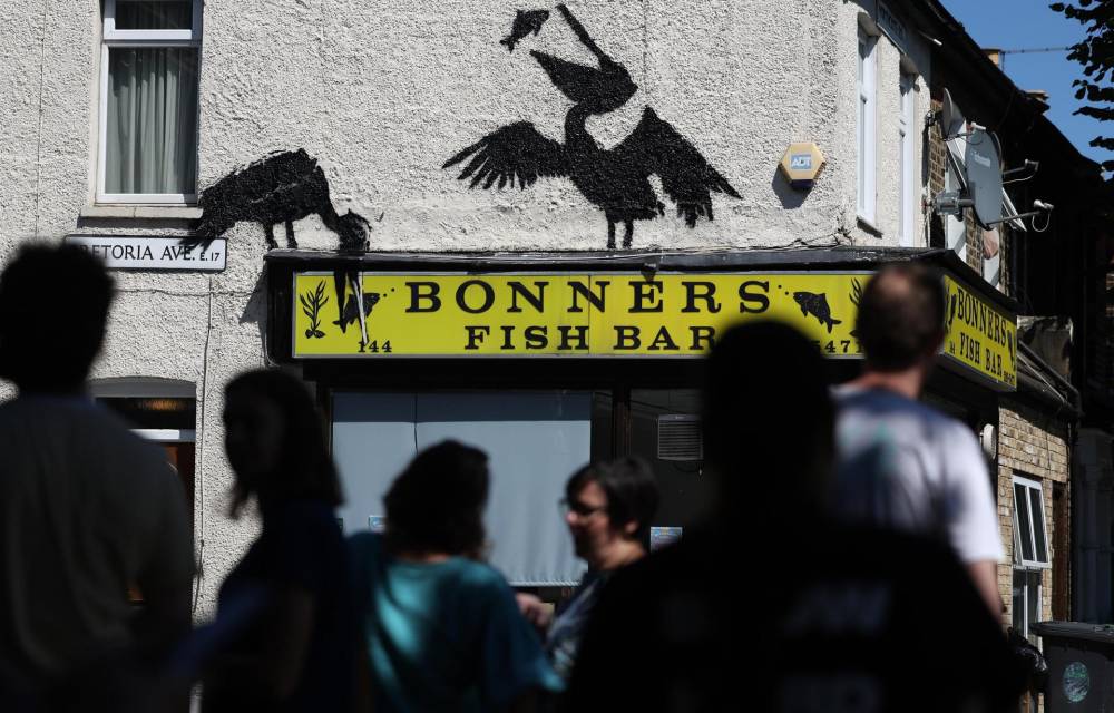 La gente observa una obra de arte recientemente confirmada de Banksy en el costado de una tienda de pescado y papas fritas en Walthamstow en Londres, Gran Bretaña, el 9 de agosto de 2024. Es la quinta obra de arte animal confirmada de Banksy en el espacio de cinco días. (Reino Unido, Londres) EFE/EPA/ANDY LLUVIA