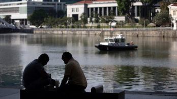 Dos hombres sentados junto al río Singapur frente a la Casa del Parlamento.