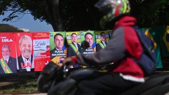Un motociclista fue captado este 30 de septiembre al pasar frente a una venta informal de banderas con la imagen del presidente de Brasil y candidato a la reelección, Luiz Inácio Lula da Silva, y del máximo candidato opositor, Flávio Bolsonaro, en Brasilia (Brasil). EFE/Andre Borges