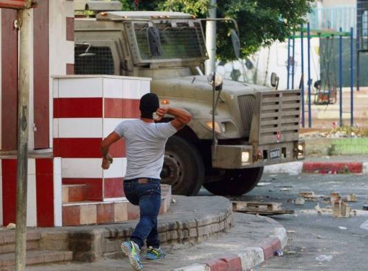 Un palestino lanza una piedra hacia una vehículo israelí durante los enfrentamientos con palestinos en una operación de madrugada, en la ciudad cisjordana de Jenin.