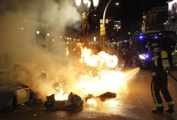 Miembros del cuerpo de bomberos sofocan las llamas de los contenedores de basura incendiados en el Paseo de Gracia de Barcelona.