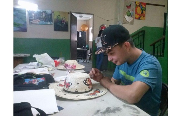 En un rincón de su hogar elabora las pinturas de los sombreros.