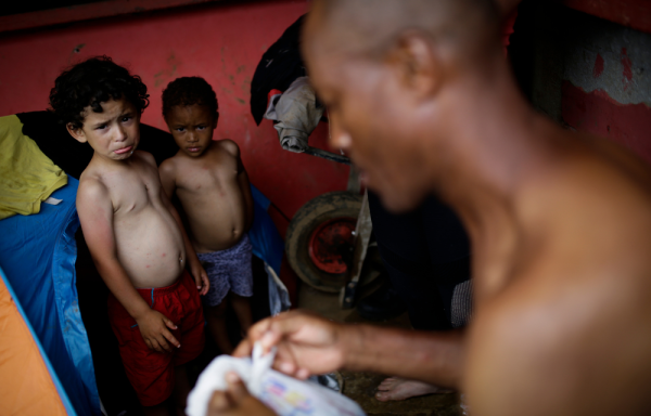 Los hermanos venezolanos Cristián Pernalete (i), de 4 años, y Carlos Méndez (c), de 2, descansan junto a su padre, el ecuatoriano Carlos Alfonso Méndez, de 56 años, el 13 de octubre de 2022, en el pueblo de Bajo Chiquito (Panamá).