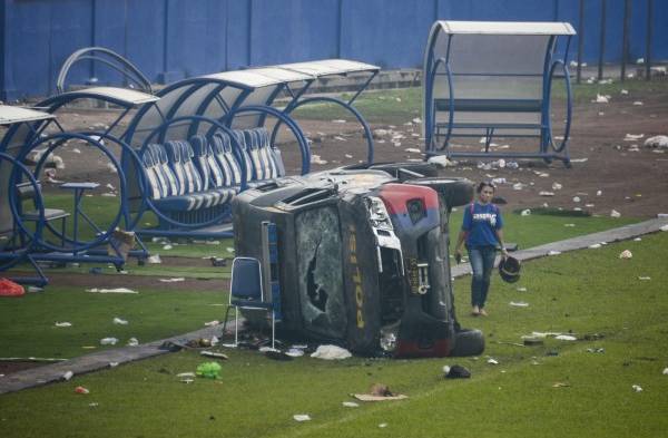 Una mujer pasa junto a un vehículo de la policía destrozado tras los disturbios en un partido de fútbol en el estadio Kanjuruhan de Malang, que dejaron 135 muertos.