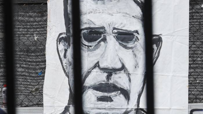 Personas caminan frente a un cartel con la imagen del expresidente de Colombia Álvaro Uribe, instalado por detractores del expresidente, afuera del Complejo Judicial de Paloquemao este lunes.