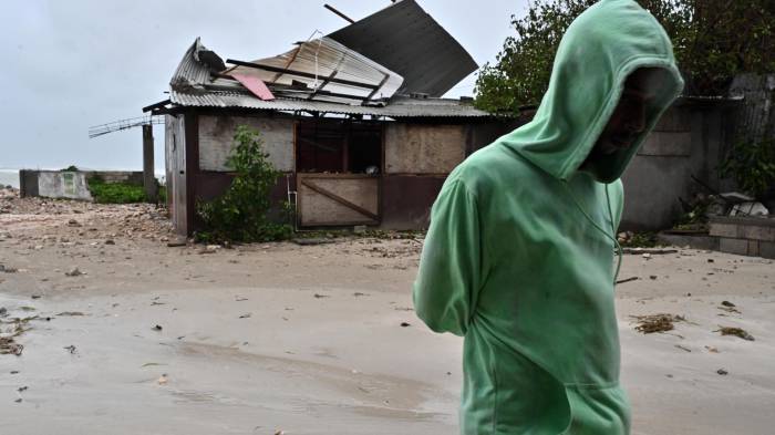 Una persona camina frente a una casa afectada por los vientos preliminares del huracán Melissa.