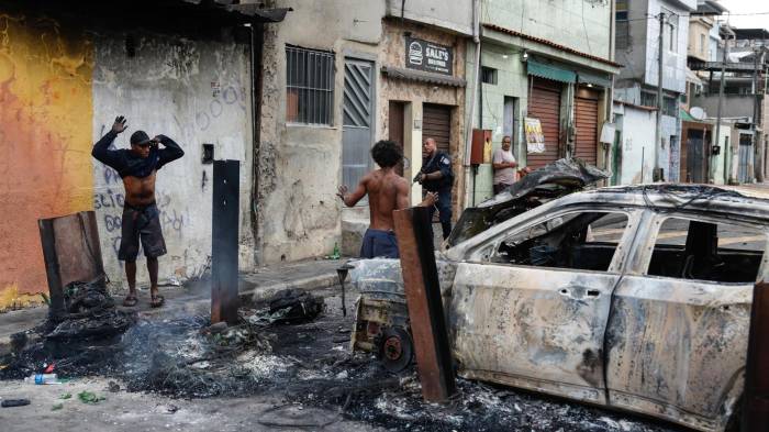 Un integrante de la Policía de Río de Janeiro custodia a dos personas durante un operativo este martes, en Río de Janeiro (Brasil).