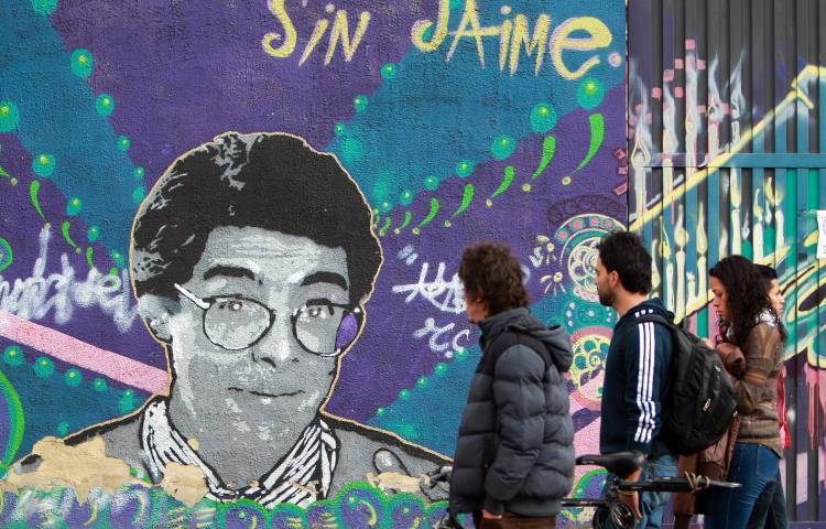 Fotografía de archivo del 13 de agosto de 2014 que muestra a un grupo de personas caminando frente a un mural con la imagen del asesinado abogado, activista por la paz y popular humorista de la televisión colombiana Jaime Garzón en Bogotá (Colombia).