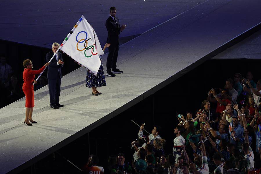 La alcaldesa de Los Angeles, Karen Bass (i), ondea la bandera olímpica, junto al presidente del COI, Thomas Bach (c).